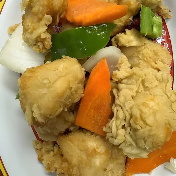 Close-up of crispy fried chicken with sliced carrots, green peppers, and onions on a white plate.