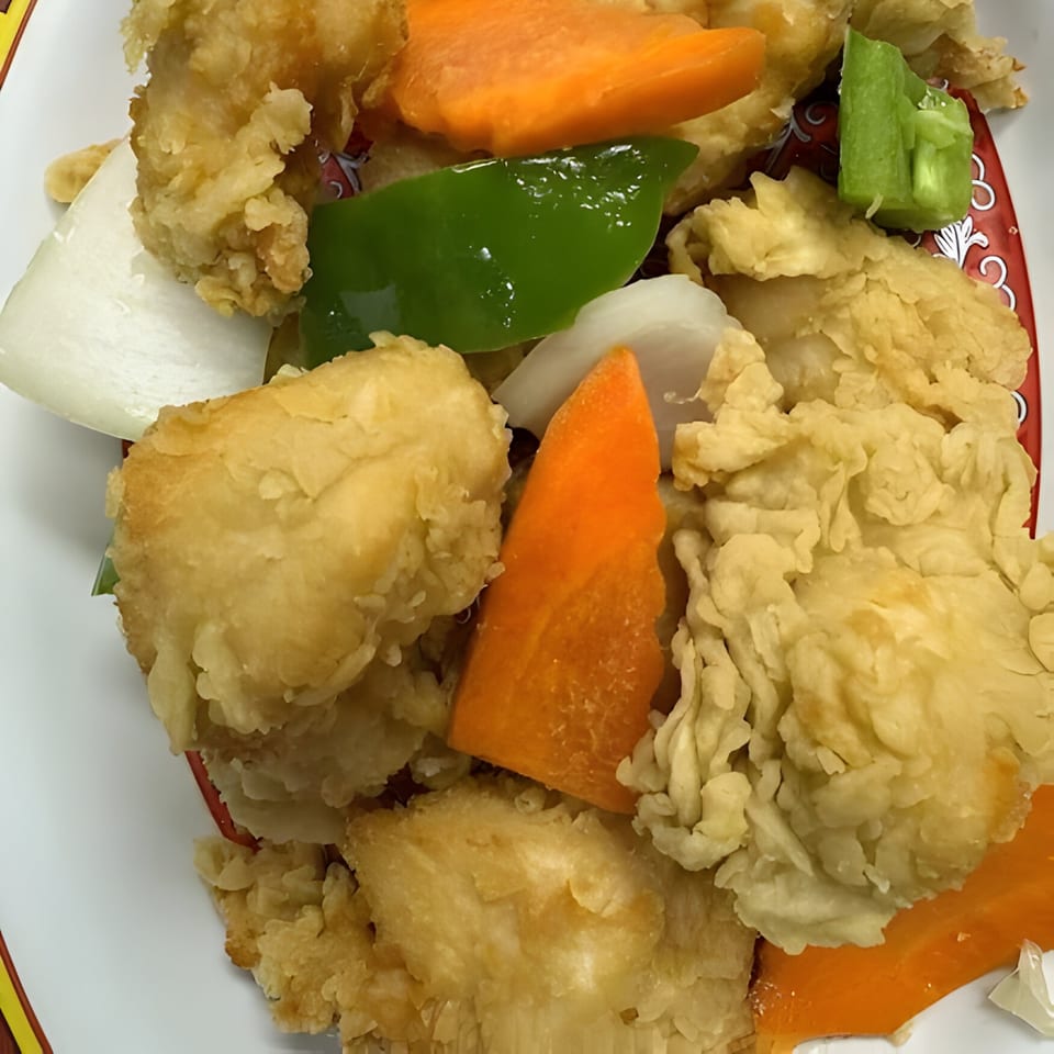 Close-up of crispy fried chicken with sliced carrots, green peppers, and onions on a white plate.