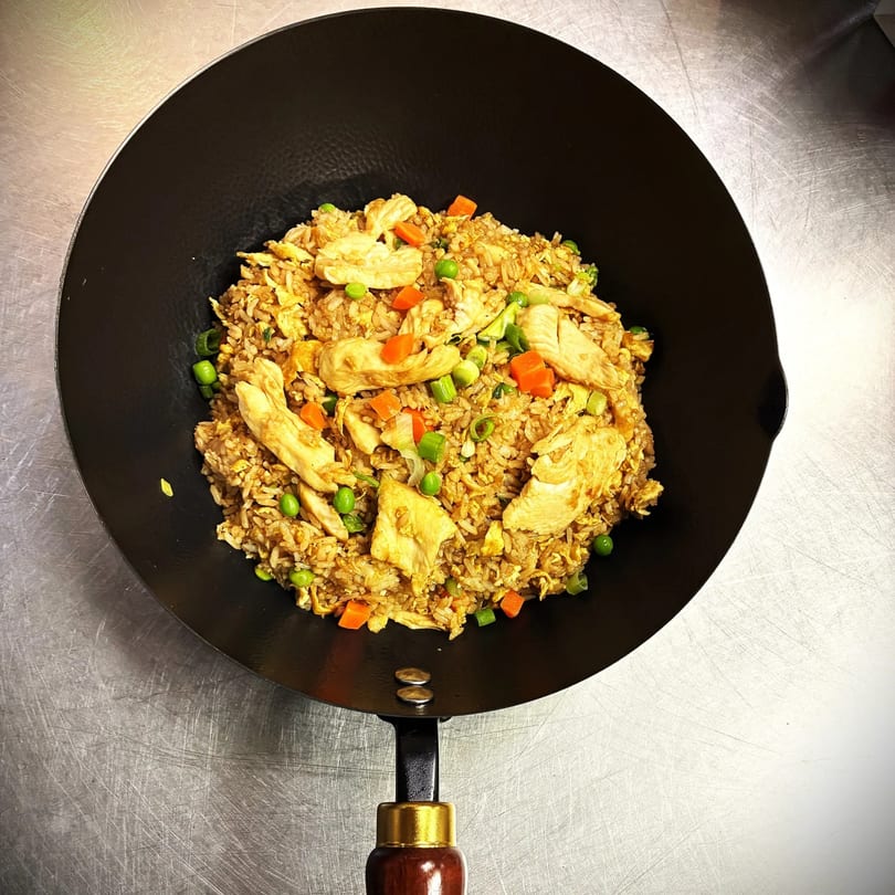 Chicken fried rice with peas, carrots, and green onions in a black wok.