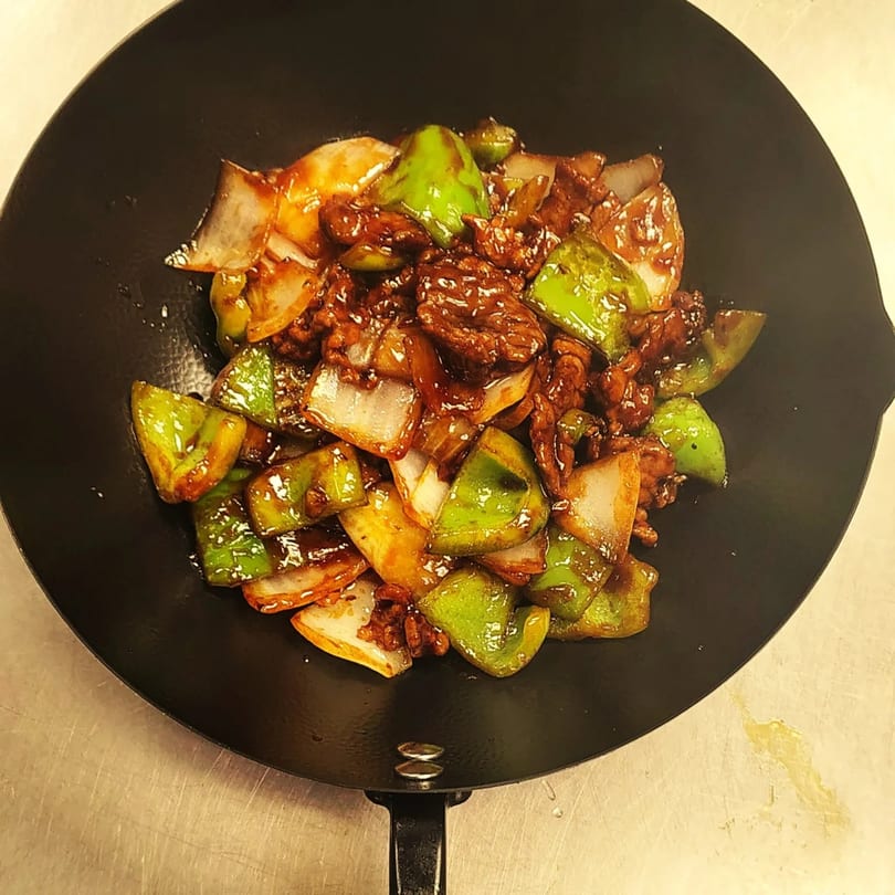 Chinese beef and peppers stir-fry with onions in a black wok from Orient Express Webb City.