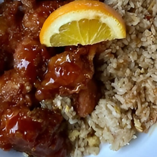 Orange chicken with fried rice and an orange slice on a white plate at Orient Express.