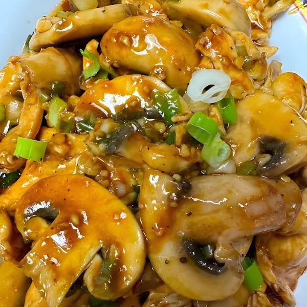 Close-up of Chinese mushroom chicken with a glossy sauce, green onions, and white onions.