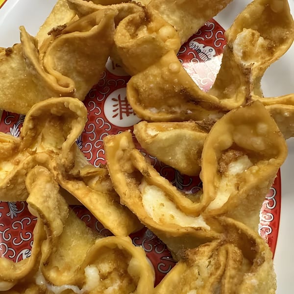 Golden-brown crab rangoon appetizers, filled with cream cheese, on a red and white patterned plate.