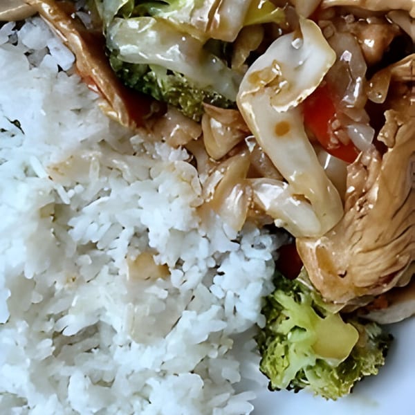 Close-up of Chinese stir-fry with chicken, broccoli, and other vegetables served over white rice.