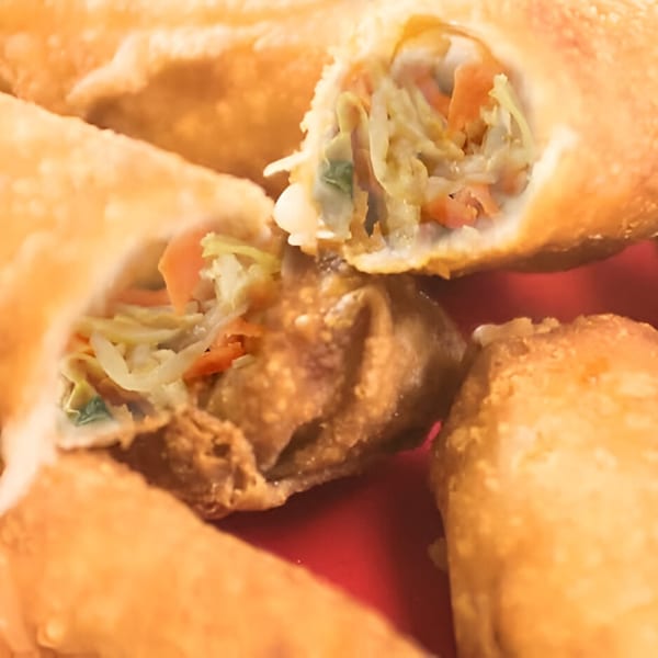 Close-up of golden-fried Chinese egg rolls, one cut open to show the vegetable filling.